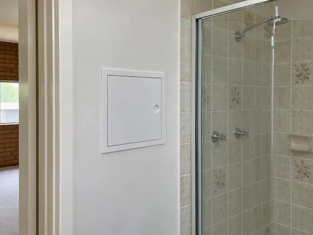 Small access panel on a painted bathroom wall beside a tiled shower in Carlingford